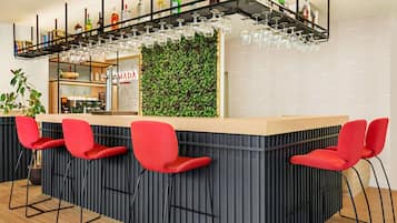 Zona de bar con mostrador, taburetes rojos y estante empotrado con botellas y vasos.