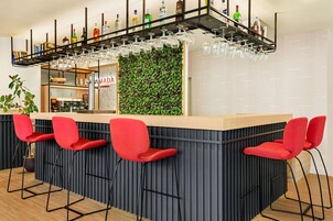 Zona de bar con mostrador, taburetes rojos y estante empotrado con botellas y vasos.