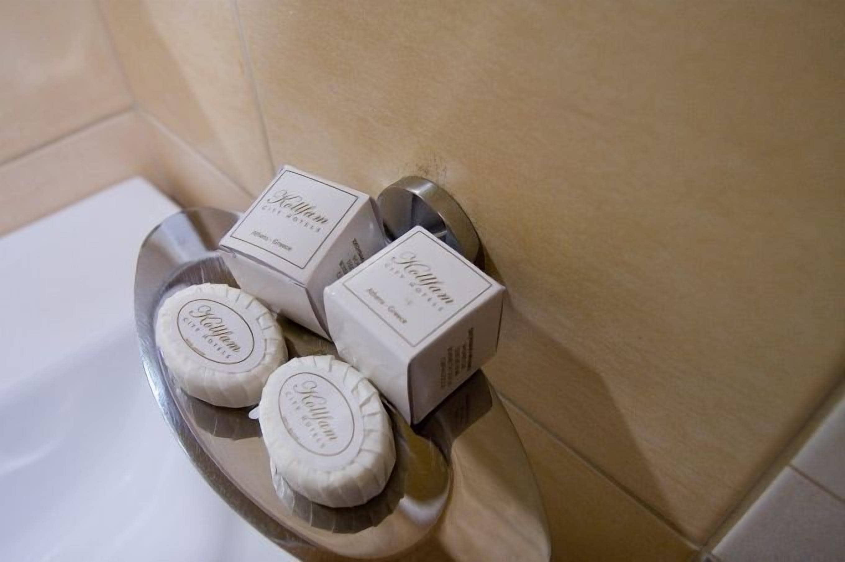 Un bagno con una parete piastrellata color beige, una vasca da bagno bianca e tre saponette bianche su un vassoio d'argento.