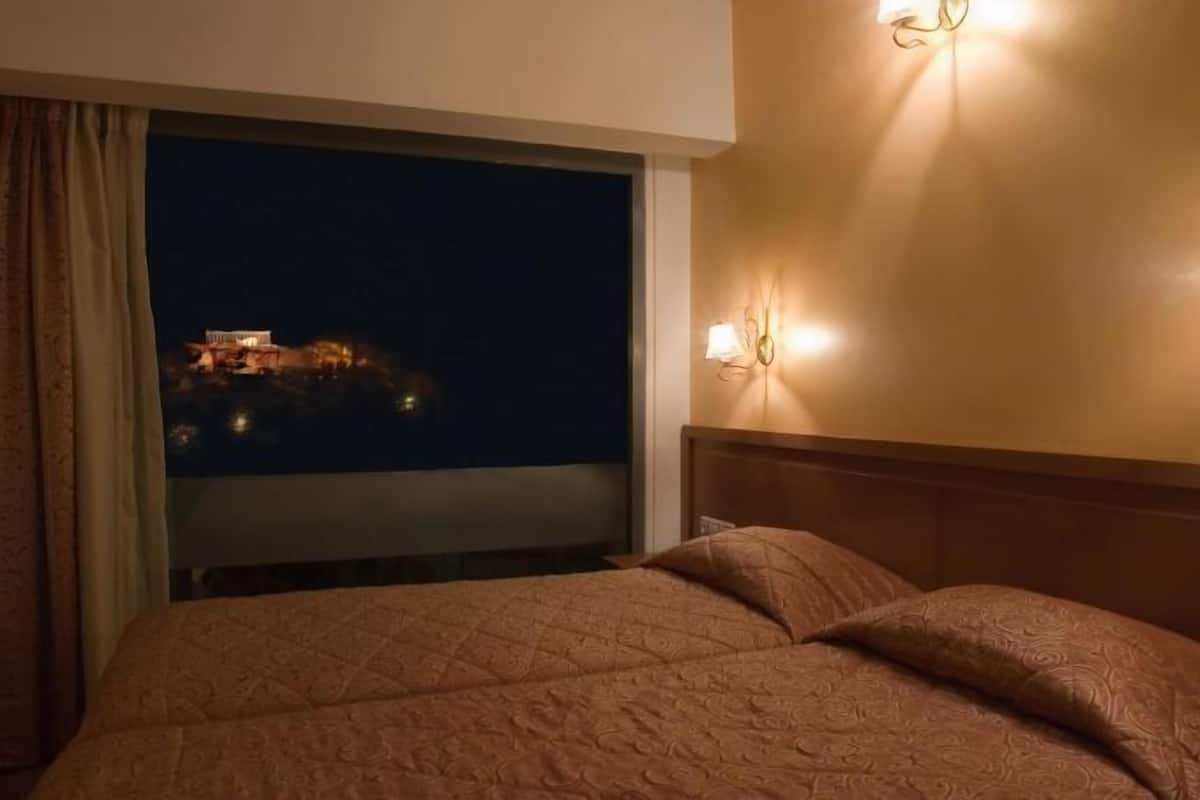 A hotel room with a large bed, a night view of a building, and wall-mounted lighting.