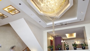 A spacious living area with dark sofas, a coffee table, and a large chandelier. - Crystal City Hotel (Athens)