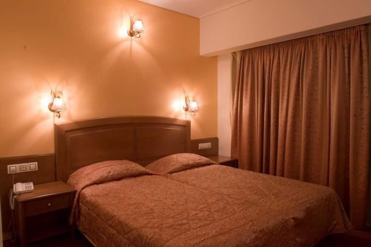 A hotel room with a wooden headboard, two bedside lamps, a telephone, and a large window with curtains.