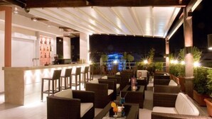 An outdoor bar area with wicker furniture, a bar counter, and a view of the cityscape at night. - Crystal City Hotel (Athens)