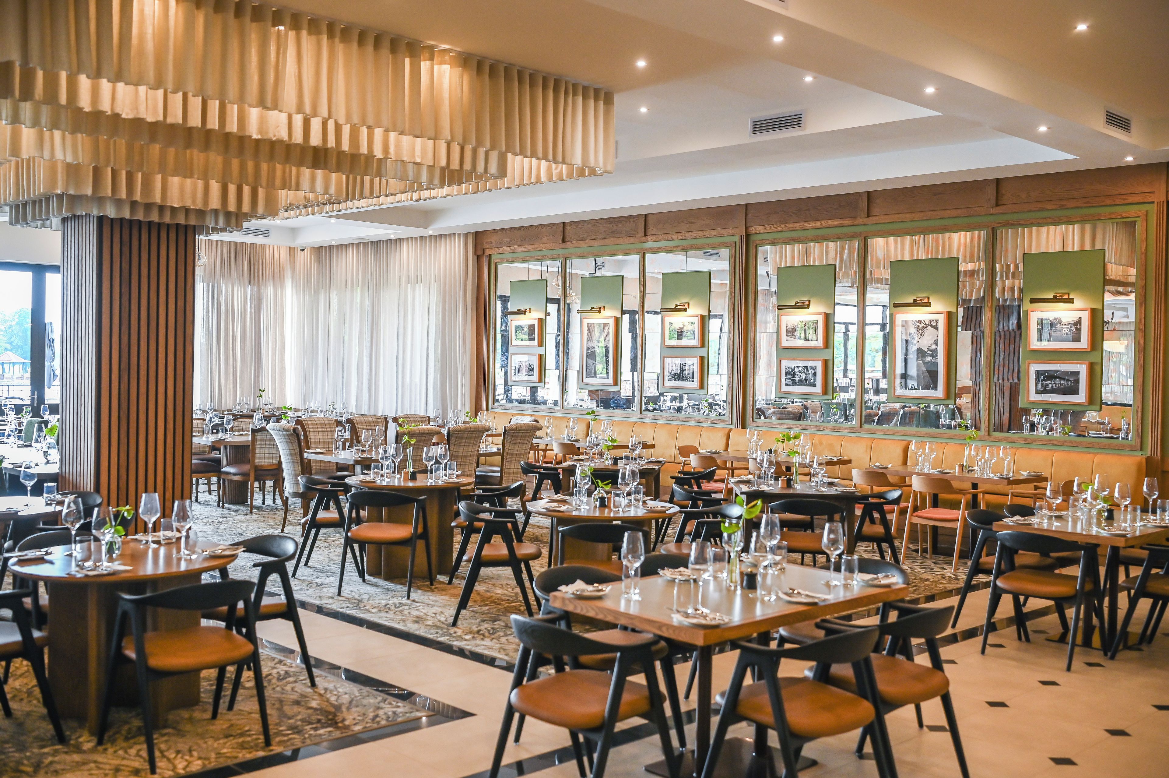 A restaurant with multiple dining tables, chairs, and a large window with framed pictures.