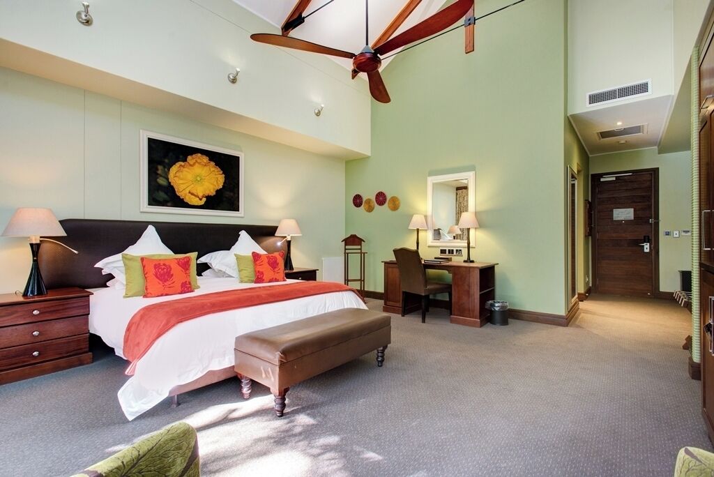 Habitación de hotel con cama, mesitas de noche, escritorio, silla, ventilador de techo y un ventanal grande.