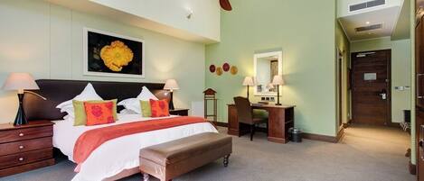 Habitación de hotel con cama, mesitas de noche, escritorio, silla, ventilador de techo y un ventanal grande.