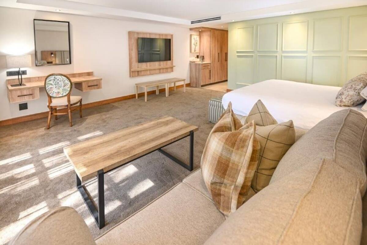 Een hotelkamer met een bed, een slaapbank, een bureau met stoel, een bankje, een spiegel en een kledingkast.