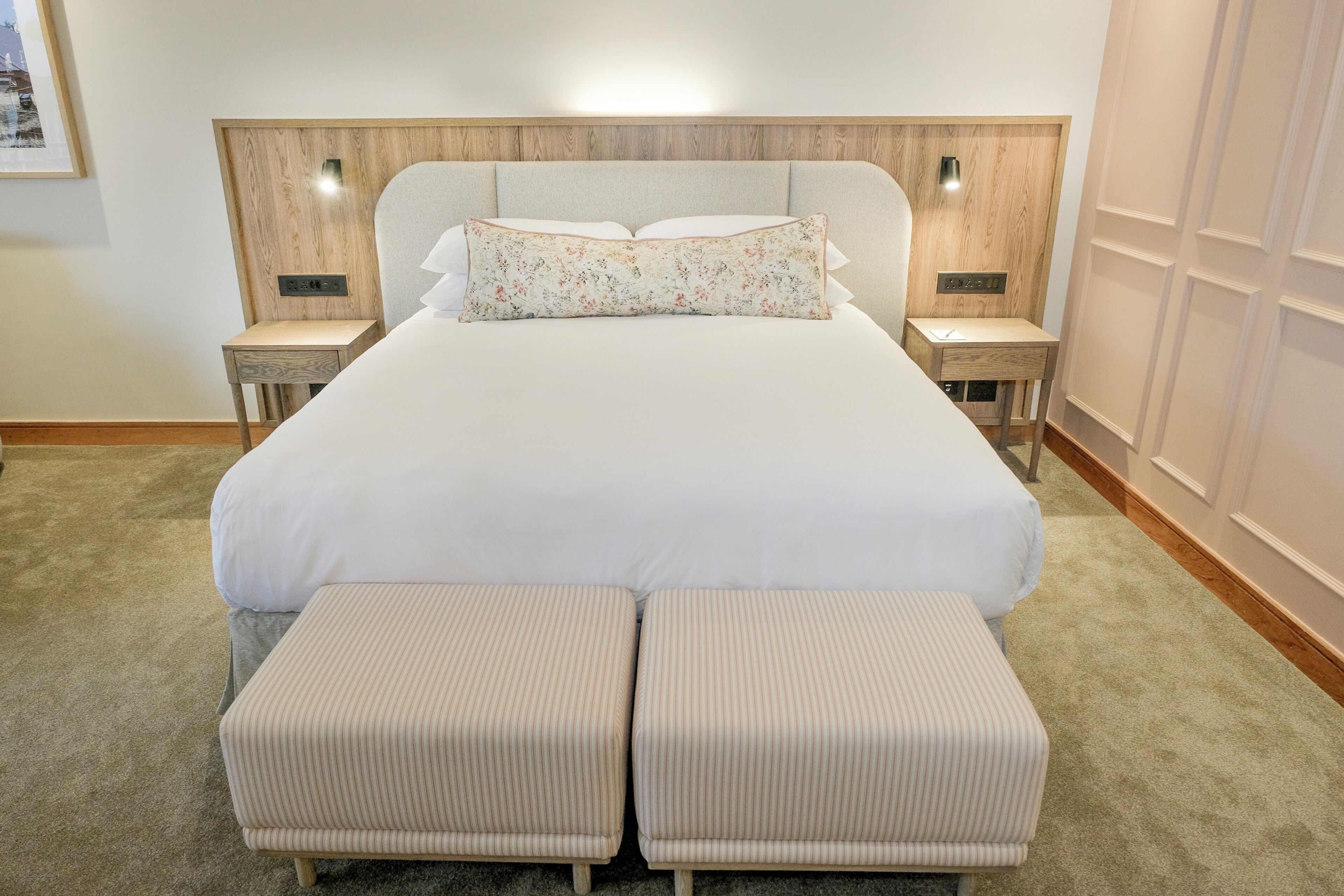 Ein großes Bett mit Kopfteil, zwei Nachttische, eine Bank und ein Teppichboden.