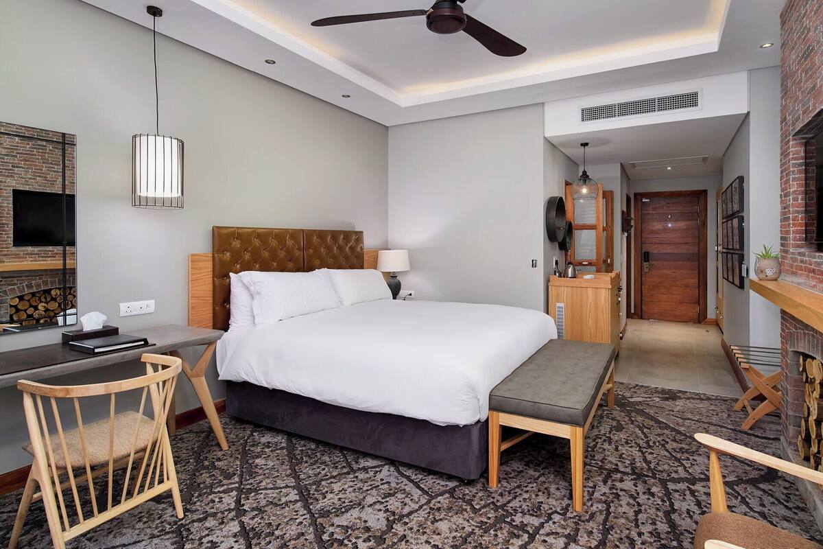Een hotelkamer met een bed, een bureau, een stoel, een televisie, een plafondventilator en een open haard.