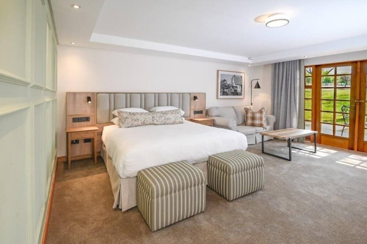 Een slaapkamer met een groot bed, twee nachtkastjes, een bank, een salontafel en uitzicht op een tuin door een schuifdeur.