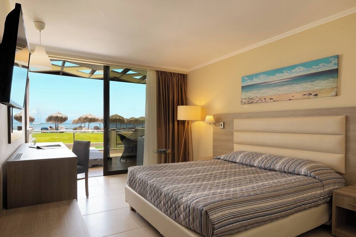 A hotel room with a bed, desk, chair, and a view of the beach.