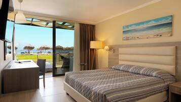 A hotel room with a bed, desk, chair, and a view of the beach.
