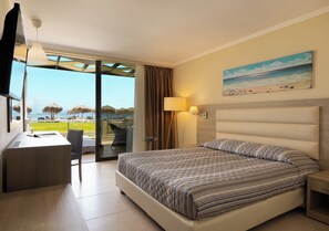 A hotel room with a bed, desk, chair, and a view of the beach.