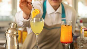 Um bartender preparando bebidas com um coqueteleira, um coquetel amarelo e uma bebida de laranja.