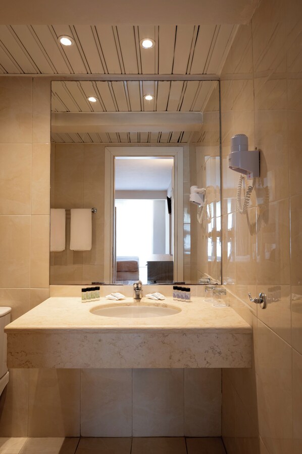 Une salle de bain moderne avec un grand miroir, un lavabo et un sèche-cheveux fixé au mur.
