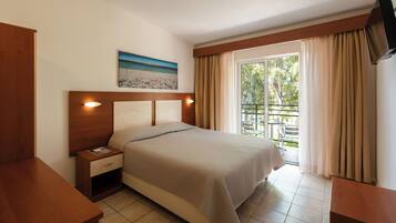 Habitación de hotel con cama, mesita de noche, un cuadro de una playa, balcón con cortinas y televisor montado en la pared.