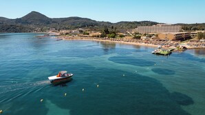 Una zona costera con un bote en el agua, una playa con sombrillas y un gran hotel al fondo.