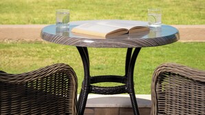 Una mesa redonda con dos sillas de mimbre, un libro y dos vasos de agua con limón.