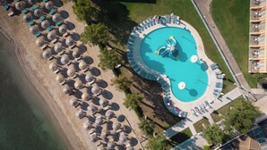 Vista aérea de un complejo turístico con una piscina central, tumbonas y sombrillas de paja.
