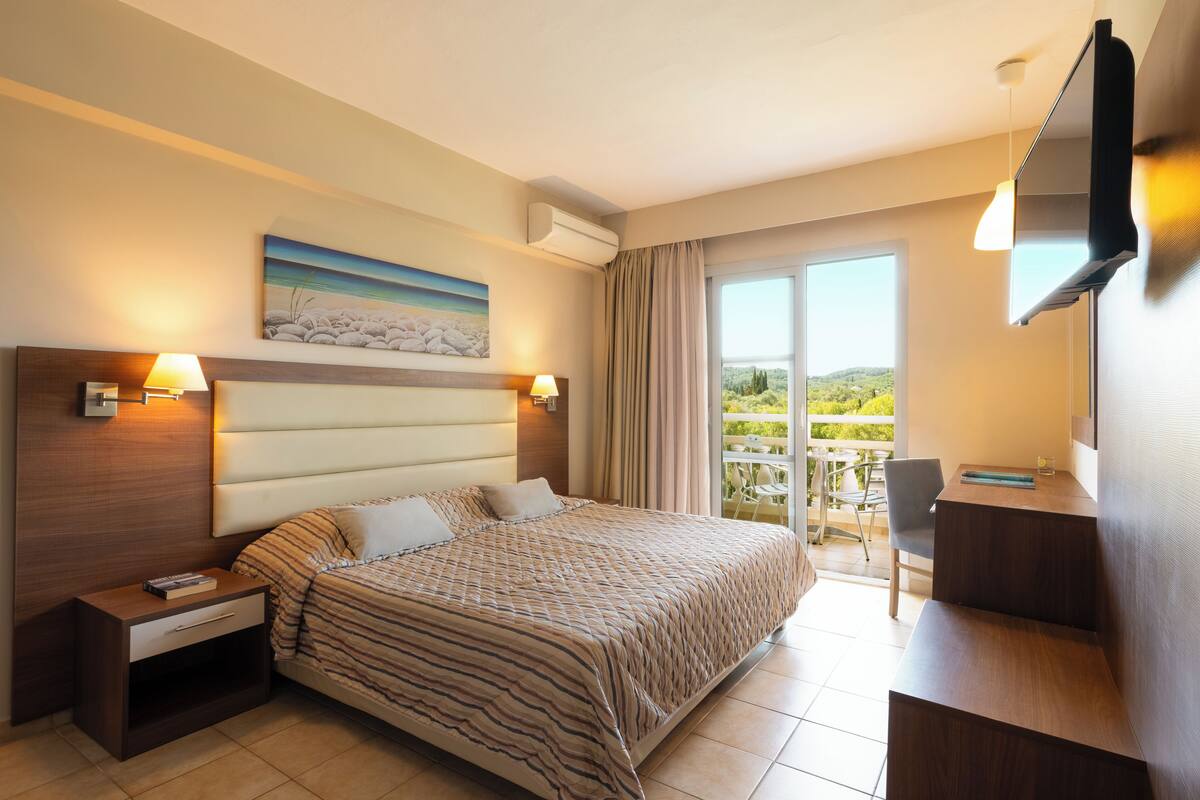 A hotel room with a bed, bedside tables, a desk, and a large window with a view.
