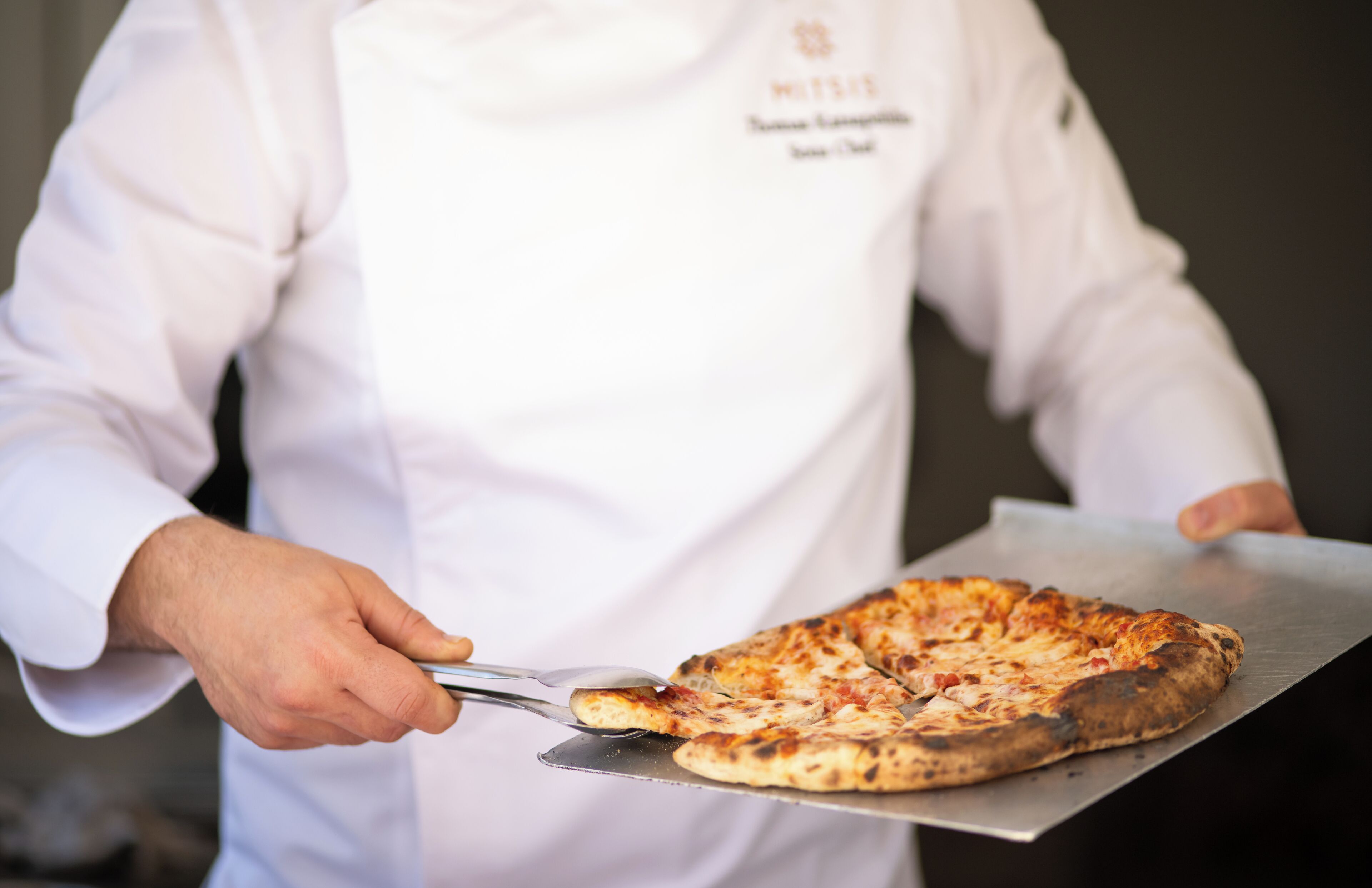 A chef holding a pizza on a metal tray.