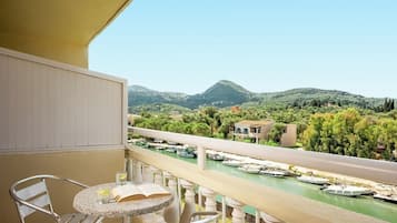 Un balcón con mesa y sillas, con vista a un río con barcos y un paisaje montañoso.