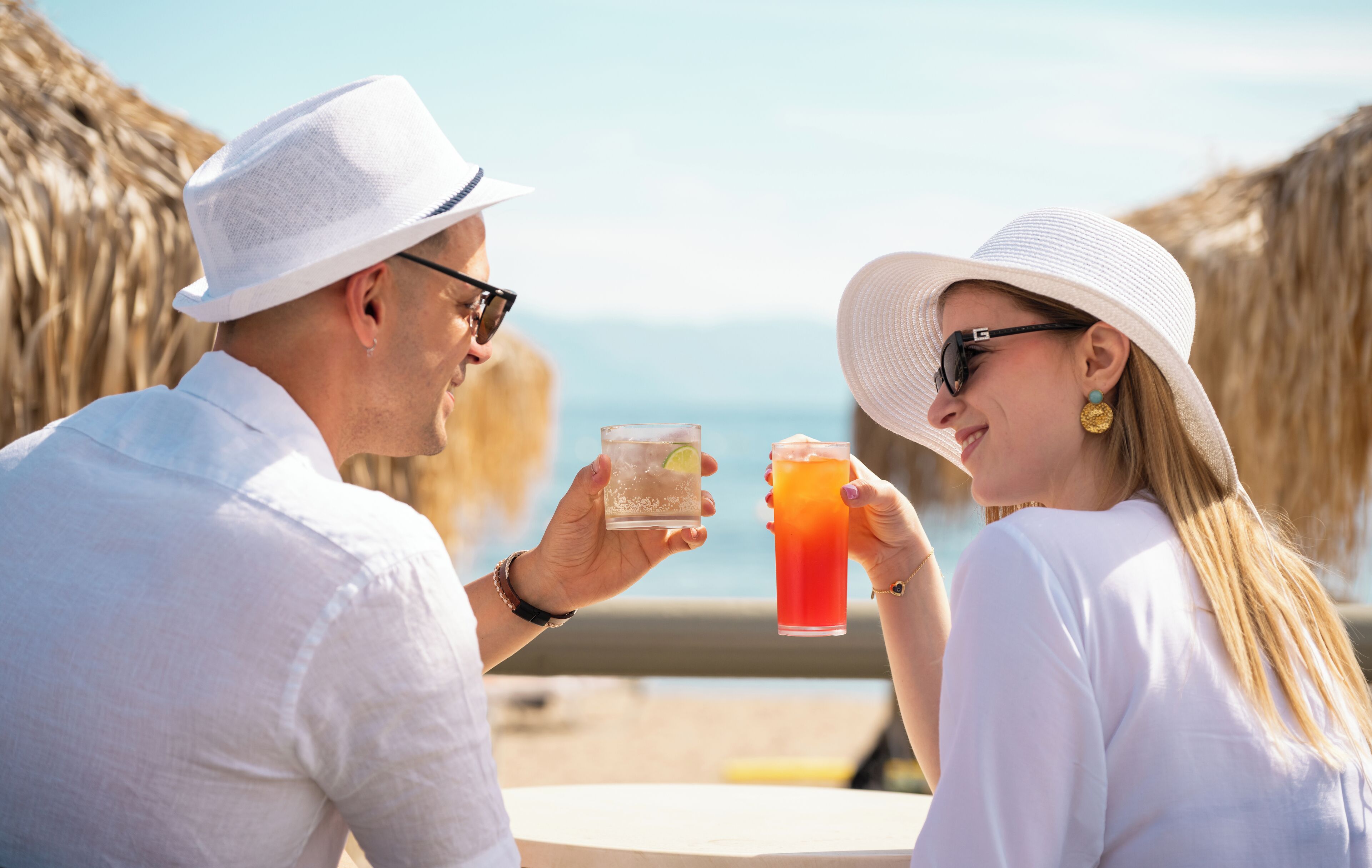 A couple toasting with drinks at a table with a view of the sea.
