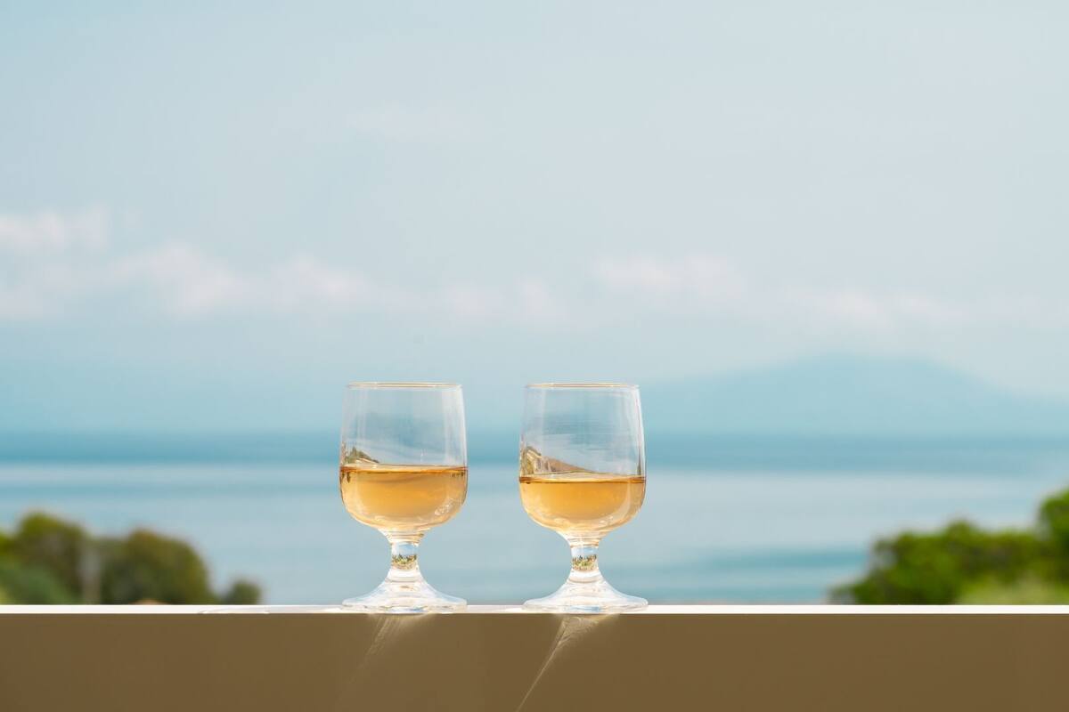 Two glasses of white wine on a balcony with a view of the sea and mountains.