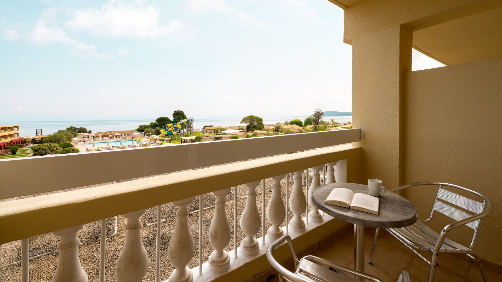 Un balcon donnant sur une piscine, avec une chaise, une table et un livre ouvert.