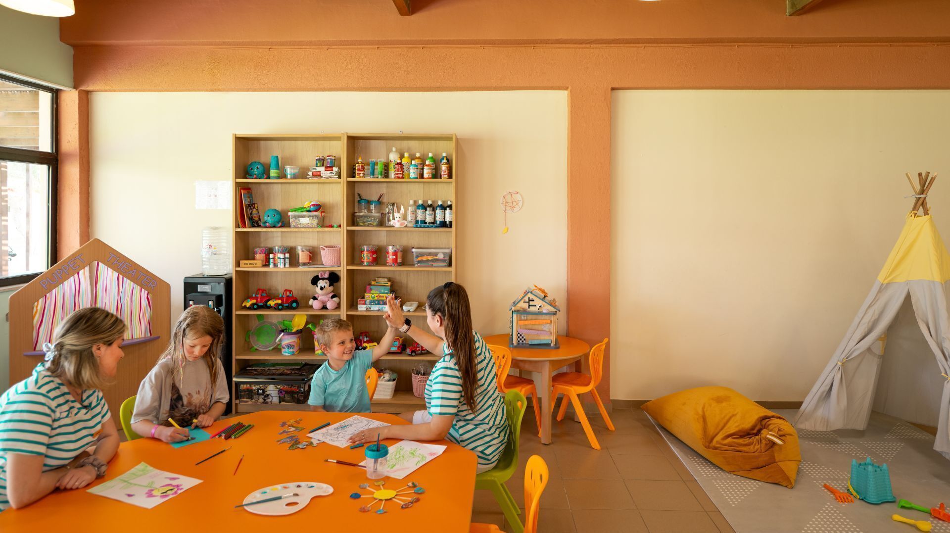 Una sala de juegos infantil con un teatro de marionetas, una casita y un tipi.