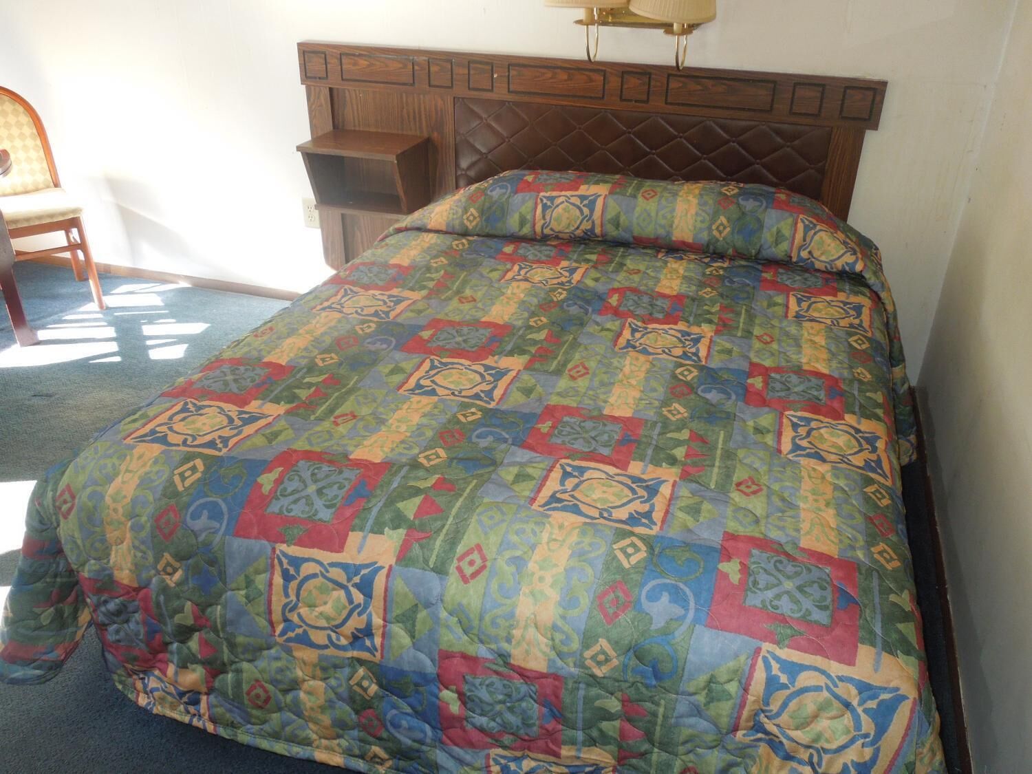A bed with a patterned quilt, a wooden headboard, and a bedside table.