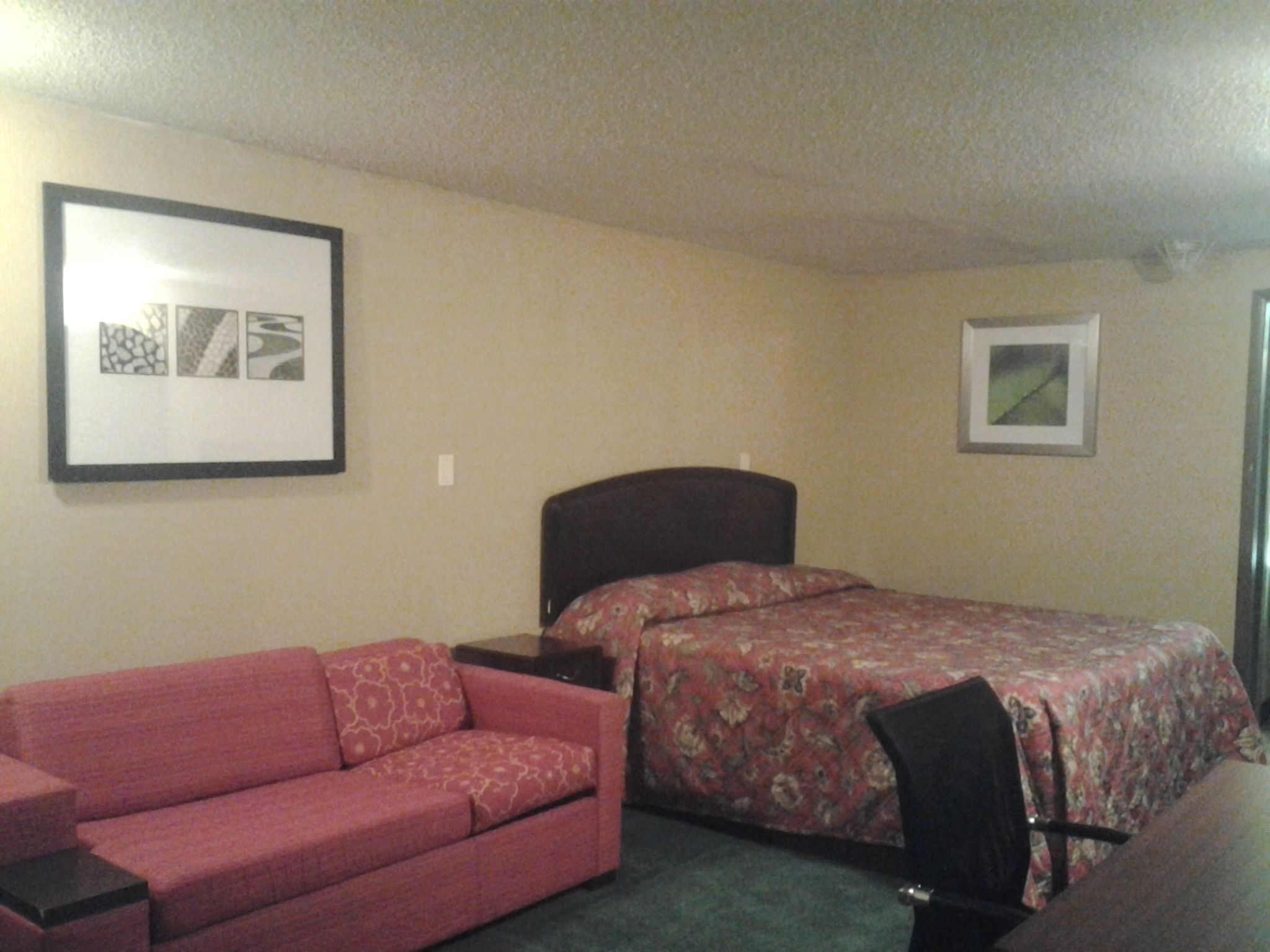 A bedroom with a bed, a red sofa, a small table, and two framed pictures on the wall.