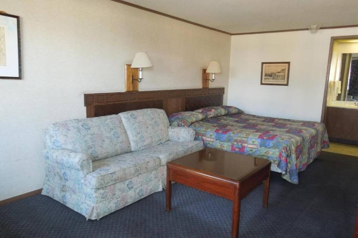 A hotel room with a bed, a sofa, a small table, and two wall-mounted lamps.