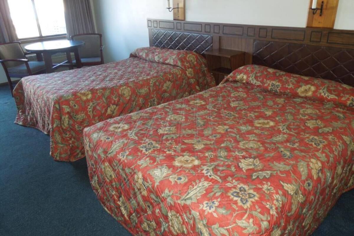 A hotel room with two beds, a small table, and a chair.