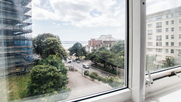 Blick aus einem Fenster auf eine Straße mit Gebäuden, Bäumen und einem klaren Himmel.