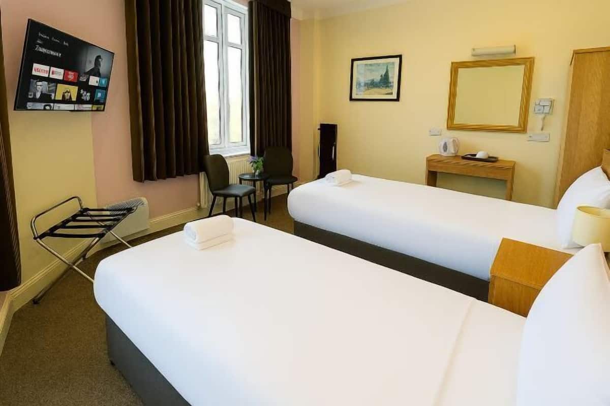 Ein Hotelzimmer mit zwei Betten, einem Schreibtisch, einem Sessel, einem Fernseher und einem Fenster mit Vorhängen.