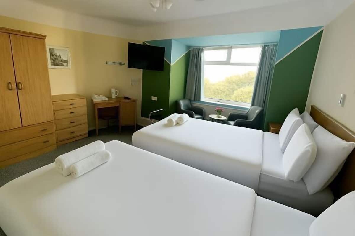 Ein Hotelzimmer mit zwei Betten, einem Schreibtisch, einem Sessel, einem Fernseher und einem Fenster mit Blick.