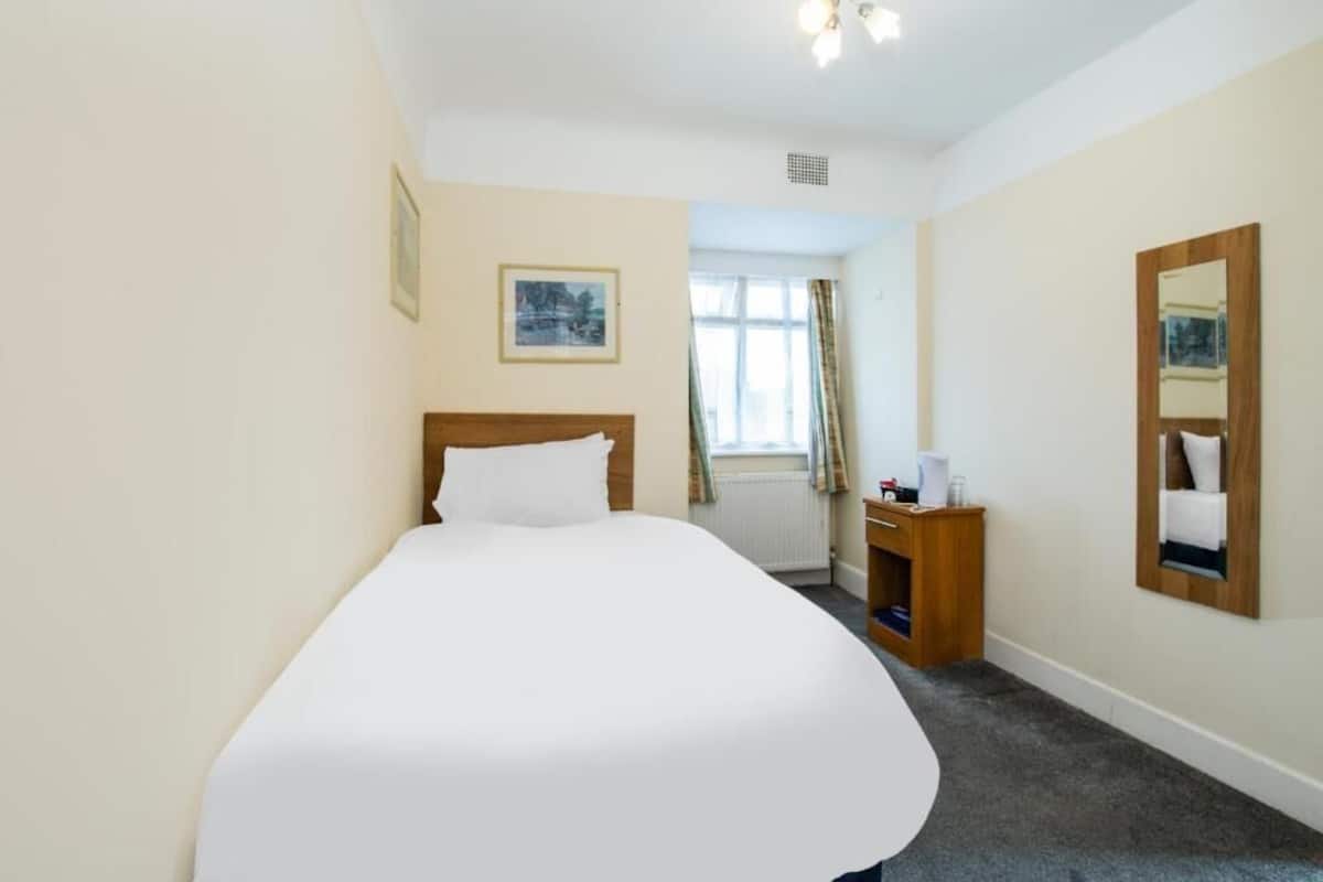 Ein Hotelzimmer mit einem großen Bett, einem Nachttisch aus Holz, einem Spiegel und einem Fenster mit Vorhängen.