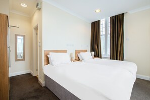 Une chambre d’hôtel avec un grand lit, une table de chevet, un miroir et une fenêtre avec des rideaux.