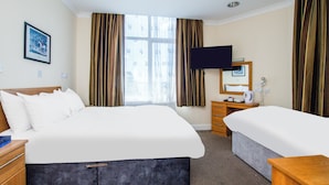 Une chambre d’hôtel avec un grand lit, un plus petit lit, un bureau avec une chaise, une télévision et une fenêtre avec des rideaux.