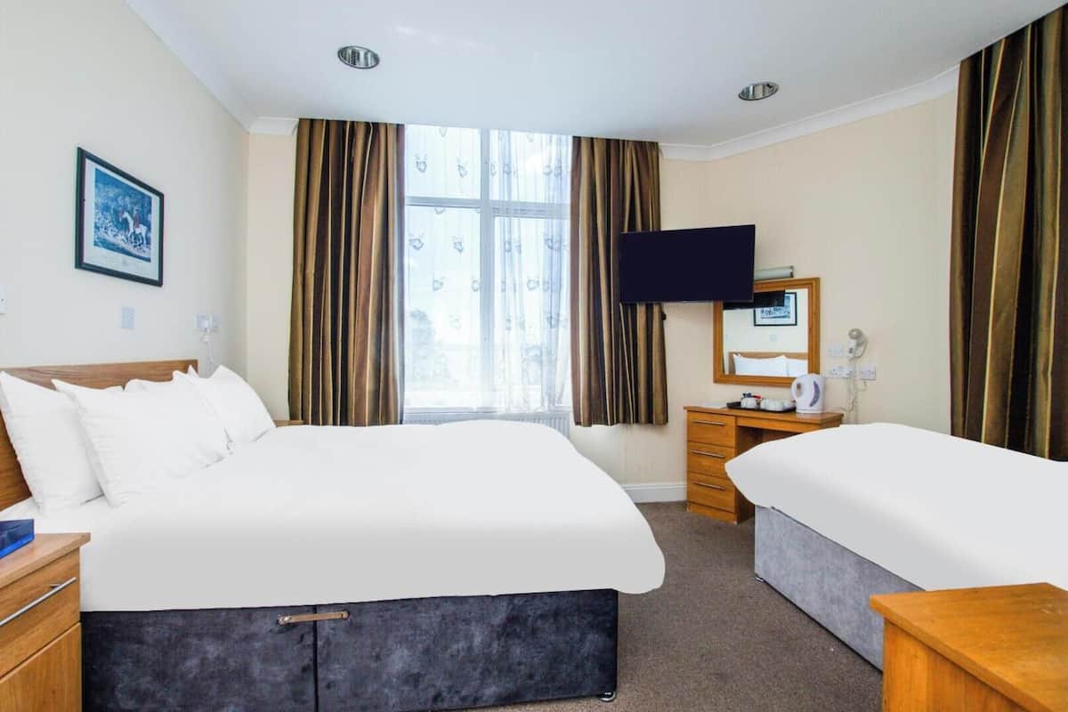 Ein Hotelzimmer mit einem großen Bett, einem kleineren Bett, einem Schreibtisch mit Spiegel, einem Flachbildfernseher und einem Fenster mit Vorhängen.