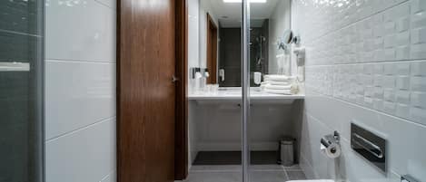 Un baño moderno con mampara de vidrio, puerta de madera, inodoro blanco, lavamanos con toallero y espejo.