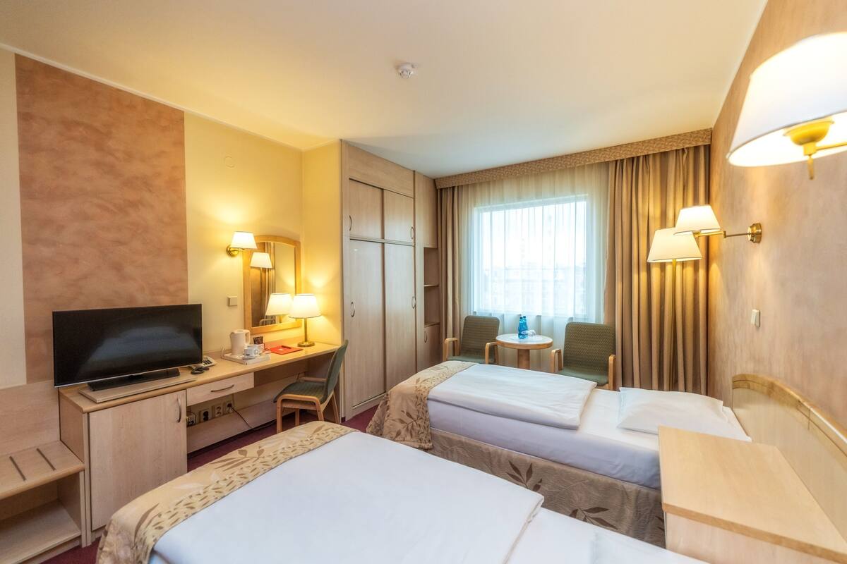Une chambre d’hôtel avec deux lits, un bureau avec une télévision, une chaise et une petite table.