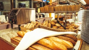 Un comptoir de buffet proposant une variété de pains et de viennoiseries, une machine à café et des piles d’assiettes.