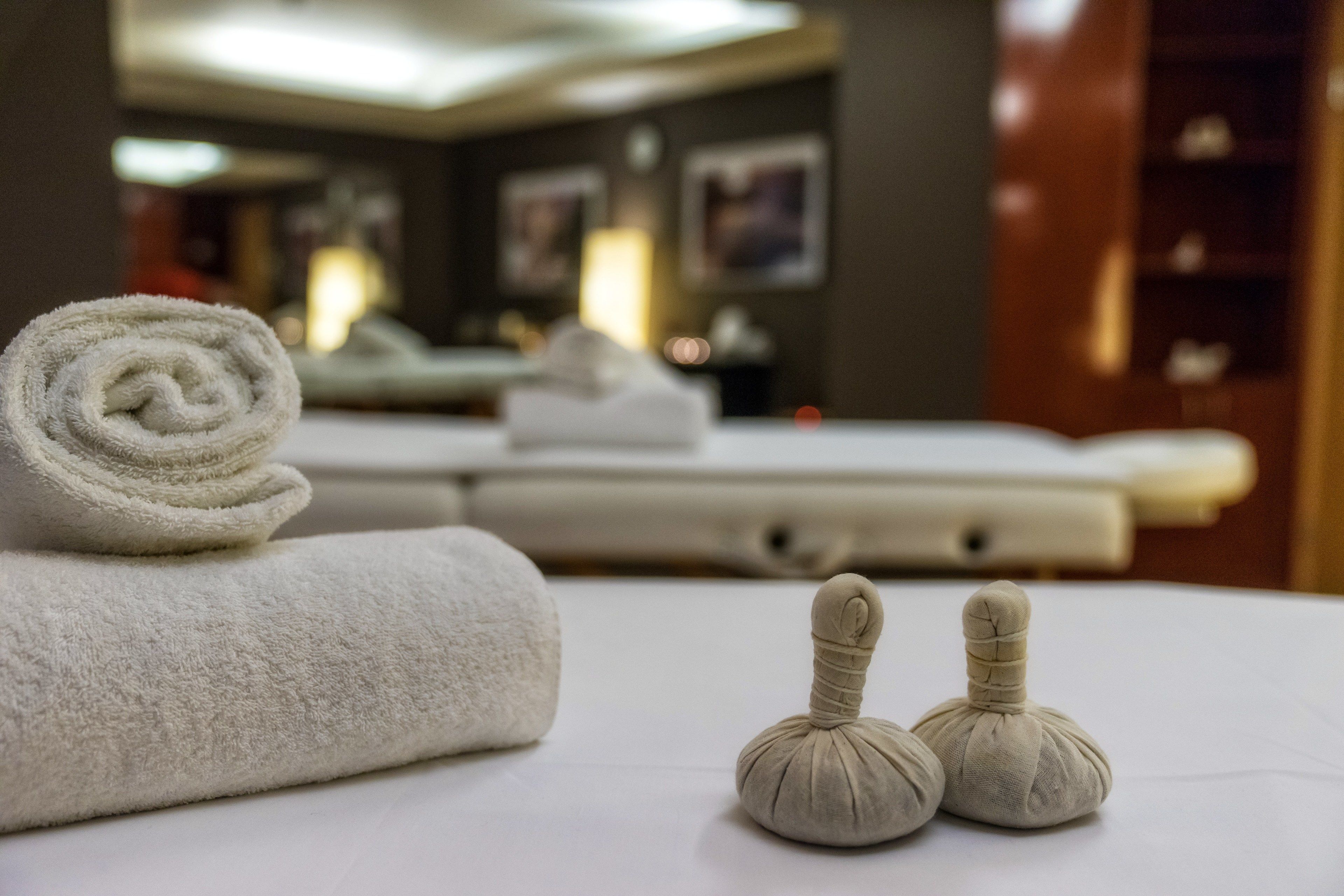 A neatly made bed with a rolled white towel and two small massage stones.