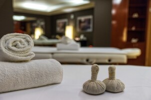 A neatly made bed with a rolled white towel and two small massage stones.