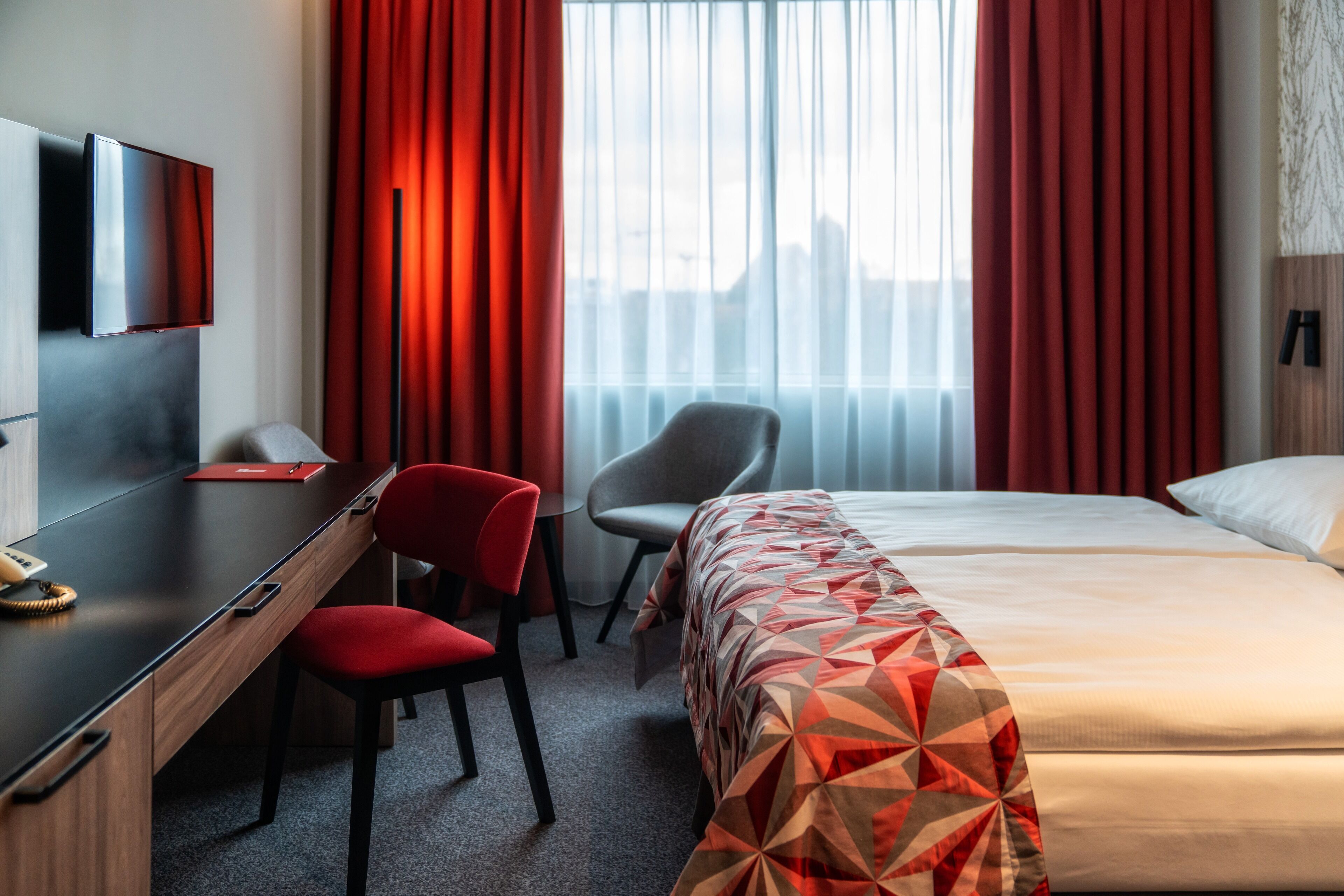 Een hotelkamer met een bed, een bureau, een stoel, een televisie en een raam met gordijnen.