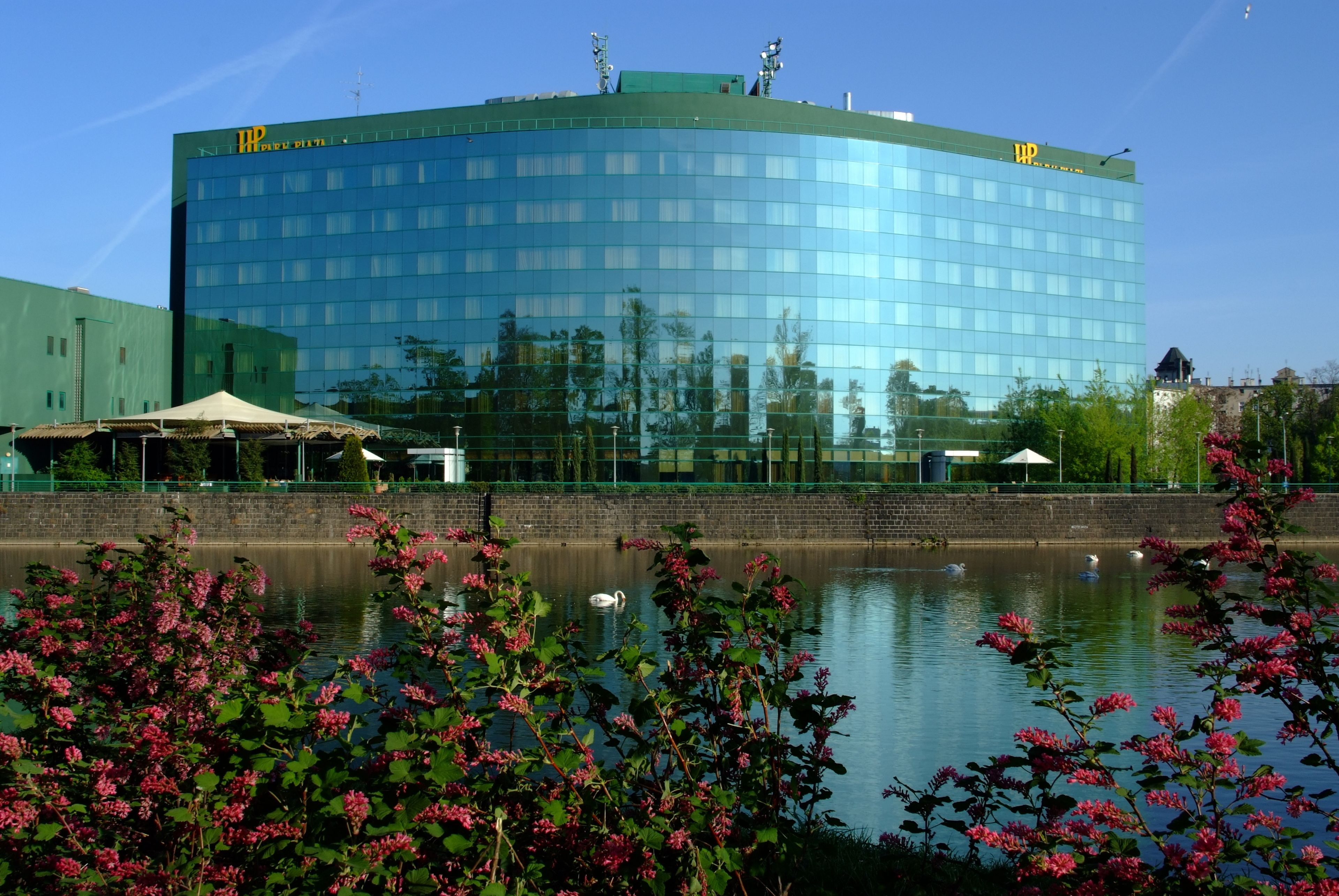A modern building with a glass facade, a green roof, and a reflection in the water.