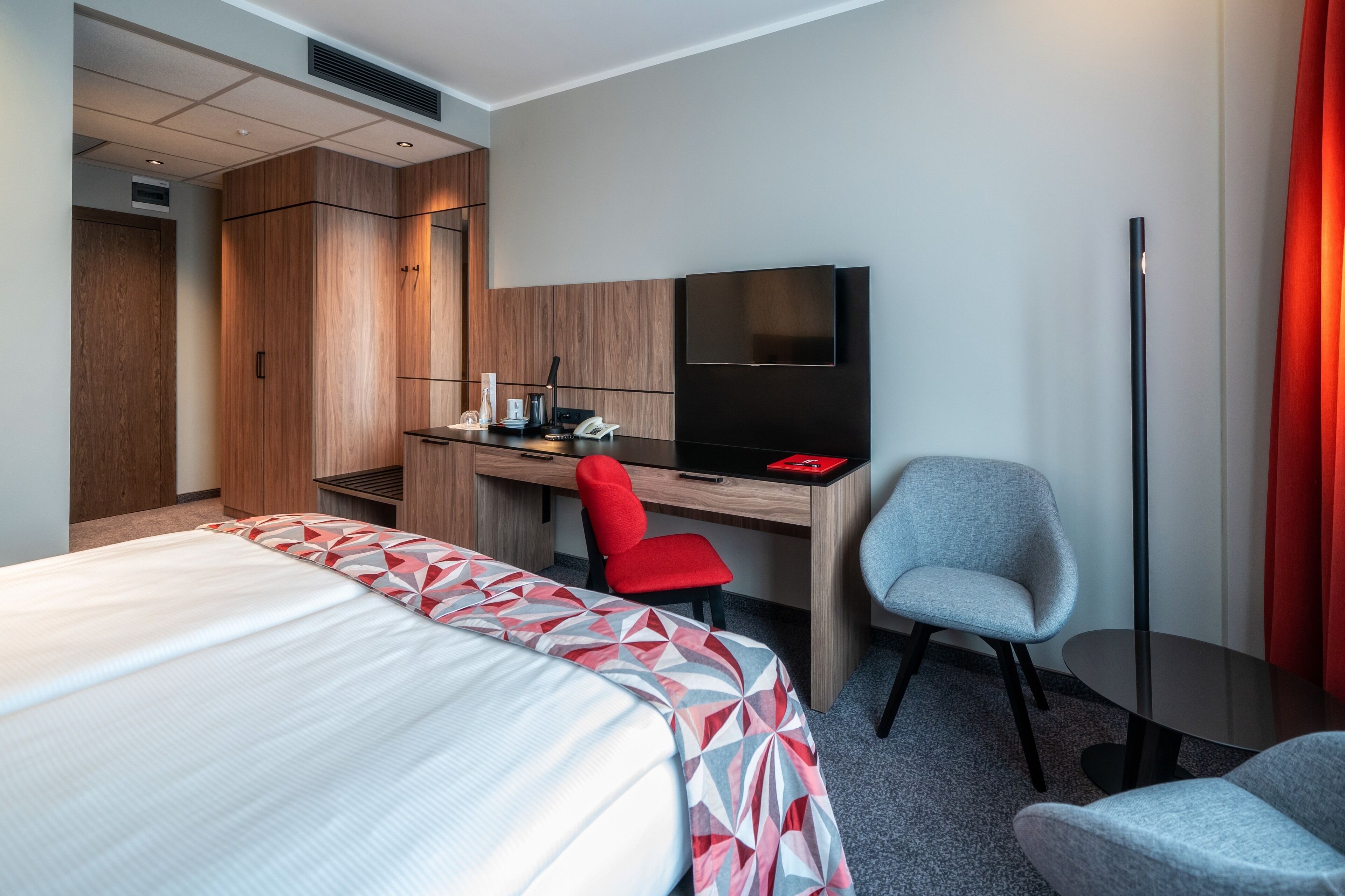 A hotel room with a bed, a desk with a chair, a television, and a wardrobe.