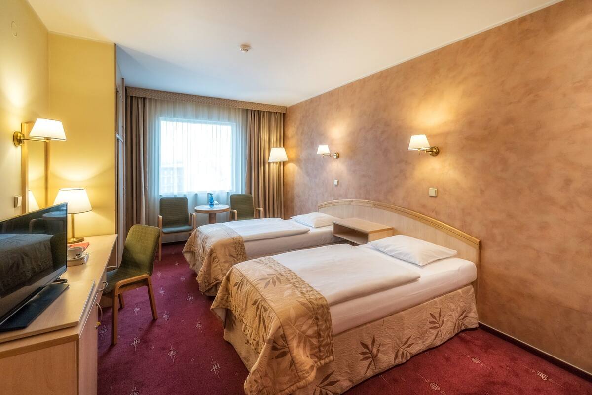 Une chambre d’hôtel avec deux lits, un bureau avec une télévision, une chaise et une petite table.